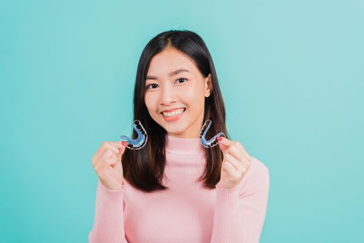 Portrait Asian beautiful young woman smiling hold silicone orthodontic retainers for teeth, Teeth retaining tools after removable braces, isolated blue background, Dental hygiene healthy care concept