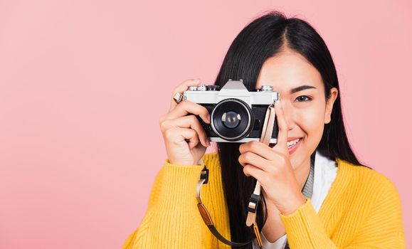 
Attractive energetic happy Asian portrait beautiful young woman smiling photographer taking a picture and looking viewfinder on retro vintage photo camera ready to shoot isolated on pink background