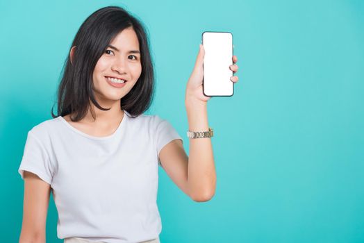 Portrait Asian beautiful happy young woman standing smile showing blank screen mobile phone looking to camera, shoot the photo in a studio on a blue background, There was copy space