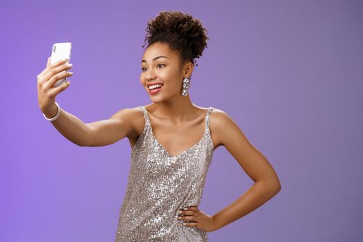 Confident glad attractive stylish millennial african-american. woman in silver glittering dress taking selfie posing cute sassy hold hand waist extend arm record video message during night-out.