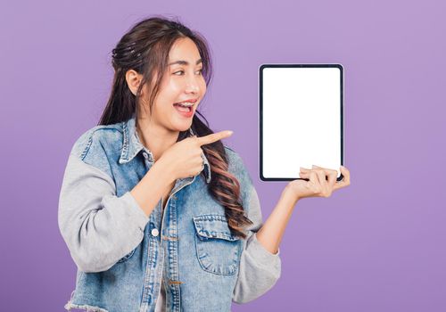 Portrait of Asian beautiful young woman confident smiling show blank screen with tablet computer and pointing, Happy lifestyle female showing digital tablet pc, studio shot isolated on purple background