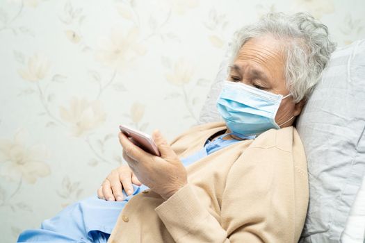 Asian senior woman patient wearing a face mask and holding mobile phone in hospital for protect safety infection and kill Novel Coronavirus Covid-19 virus.