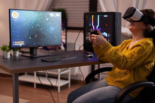 Concentrated gamer player woman with virtual reality goggles holding gaming joystick playing space shooter videogames during online competition in living room. Entertainment activities at home