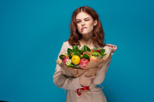 beautiful woman beige coat fruit bouquet in hands blue background. High quality photo