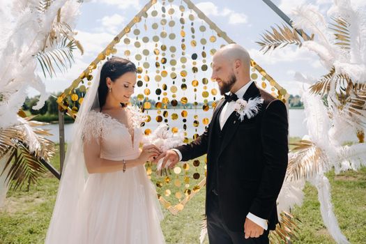 happy wedding couple near the arch wearing rings during the wedding ceremony.