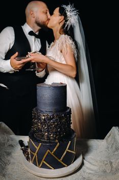 Stylish bride and groom kiss with a cake in their hands in the evening at the wedding.