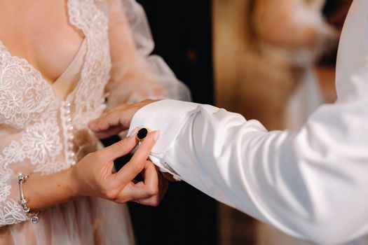 Close-up of the bride in boudoir underwear buttoning cufflinks on her sleeve