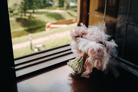 Bridal bouquet of roses decorated with white feathers on the windowsill.
