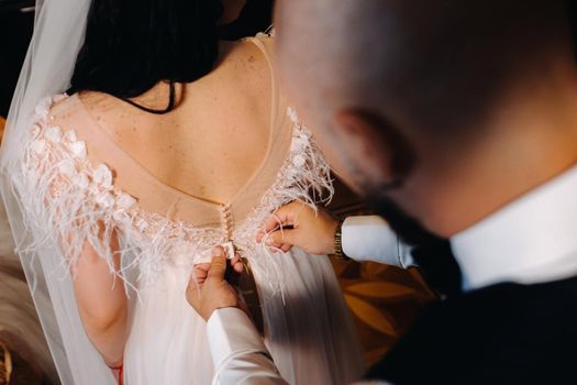 Morning of the bride. The groom helps to dress the bride in a wedding dress.