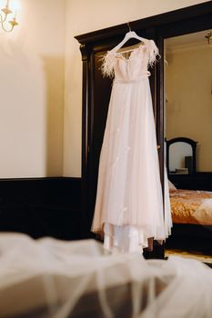 Stylish wedding dress hanging on a wooden hanger in the interior.