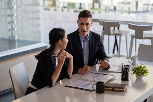 Asian and caucasian businesspeople learn new business app, apprentice listen associate tell about corporate program. Multiracial client and bank manager at business meeting using laptop negotiating.