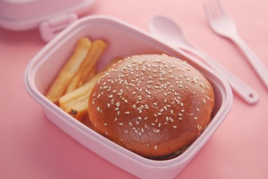 beef burger and french friend in a lunch box on pink background .