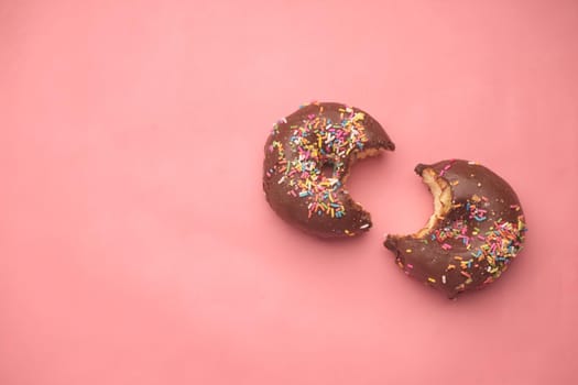 top view of half eaten chocolate donuts on pink .