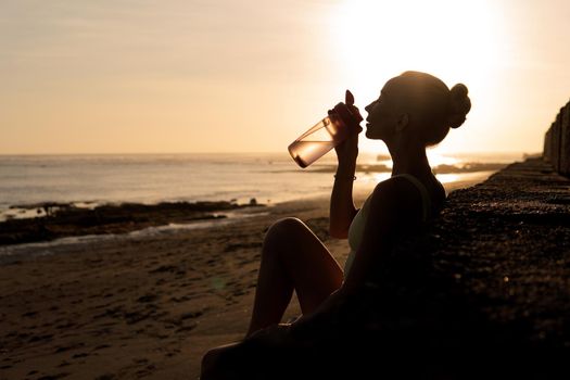 beautiful young woman drinking water. bali sunset