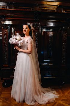 The bride in a wedding dress and with a bouquet stands at the old interior of the castle.