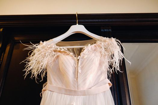 Stylish wedding dress hanging on a wooden hanger in the interior.