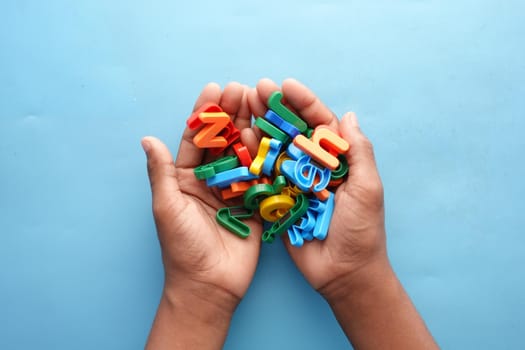 colorful plastic letters on child's hand on blue background .