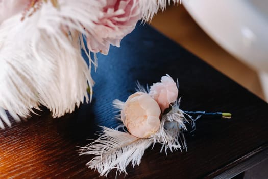 The bride's wedding bouquet of roses decorated with white feathers and a boutonniere.