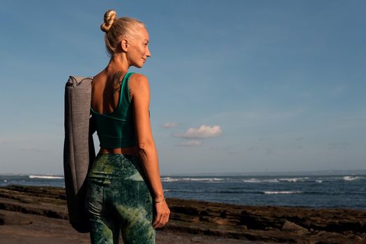 beautiful girl walking on the beach with yoga mat. bali