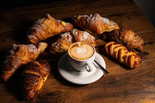 sweet croissants with cream and cappuccino on a wooden surface