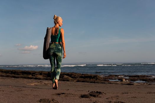 beautiful girl walking on the beach with yoga mat. bali