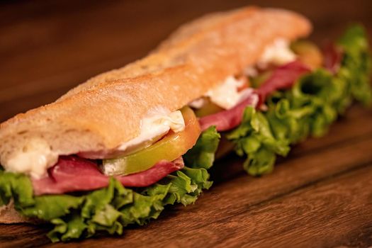 sandwich with salami and vegetables on a wooden surface