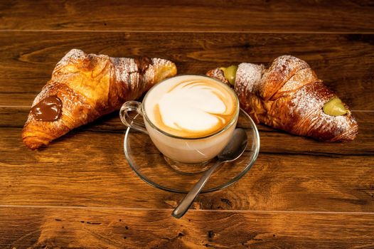 sweet croissants with cream and cappuccino on a wooden surface
