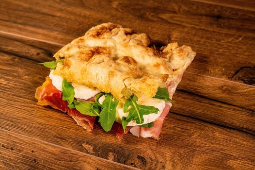 sandwich with salami and vegetables on a wooden surface
