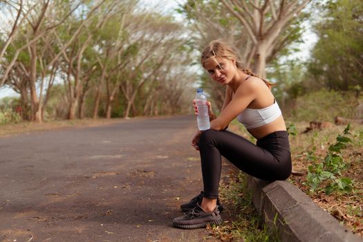 Woman in sport wear drinking water in the park. bali