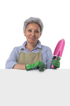Mature asian woman gardener with scoop standing behind blank banner with empty copy space for text isolated on white background