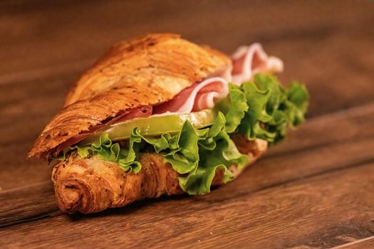 sandwich with salami and vegetables on a wooden surface