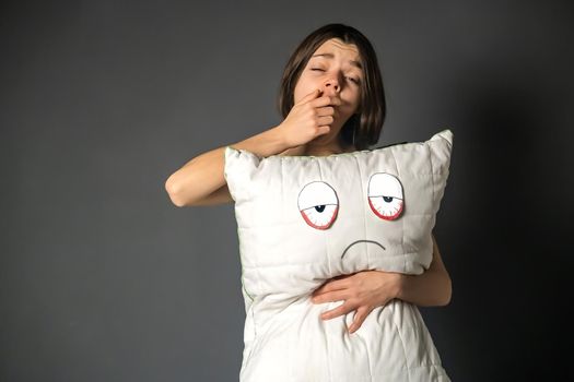 Young pretty girl just woke up in the morning with a creative pillow with painted red tired eyes.Woman with tousled hair yawning lazily and wants to sleep longer, but problems and insomnia interfere.