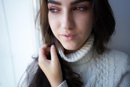 pretty woman in white sweater near the window alone. High quality photo