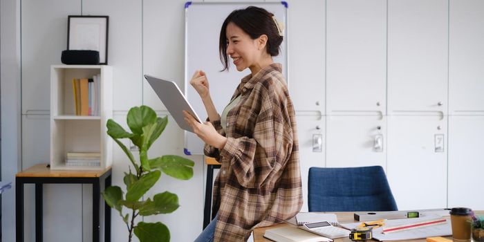 Excited asian woman sits at her workstation, ecstatic to have received a job offer following an interview by email on her laptop