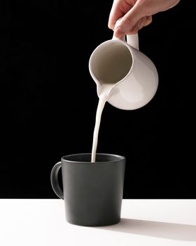 front view hand pouring milk into mug. High resolution photo