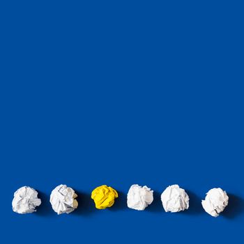 yellow crumpled paper ball among white balls against blue background. High resolution photo