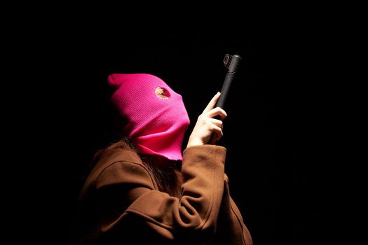 woman in a pink mask the gun crime Gangster danger the dark background. High quality photo