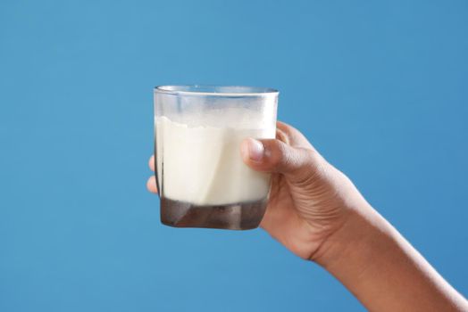 child boy hand hold a glass of milk against blue background .