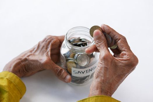senior women hand saving coins in a jar on table .