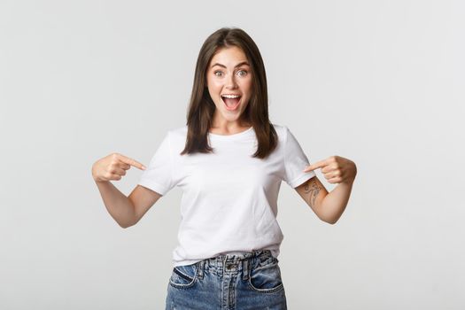 Excited happy brunette girl smiling, pointing fingers at logo, showing banner.