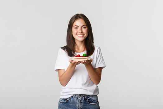 Attractive brunette girl smiling happy and holding cake on plate.