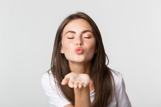 Close-up of beautiful flirty girl pouting lips and sending air kiss at camera.