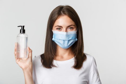 Covid-19, health and social distancing concept. Close-up of attractive smiling girl in medical mask, showing hand sanitizer, recommend antiseptic.