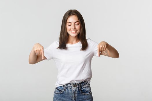 Excited happy brunette girl, looking and pointing down with satisfied smile.