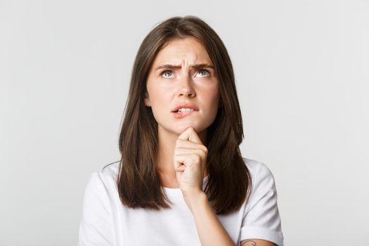 Close-up of puzzled cute thoughtful girl looking up and thinking, standing white background and pondering decision.