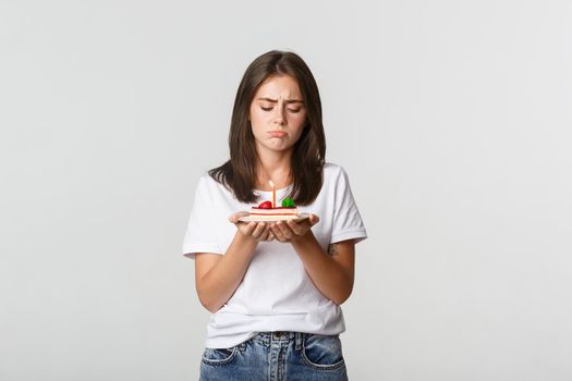 Miserable birthday girl looking sad at b-day cake with candle.