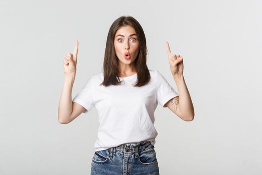 Surprised and impressed brunette girl looking amazed and pointing fingers up.