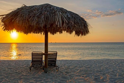 Straw umbrella at the beach on Aruba island in the Caribbean Sea at sunset