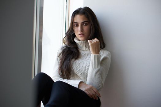 brunette in a white sweater looks out the window depression. High quality photo