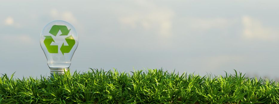 glass bulb on a ground full of vegetation with a background of clouds and a green recycling symbol inside it. copy space. 3d render